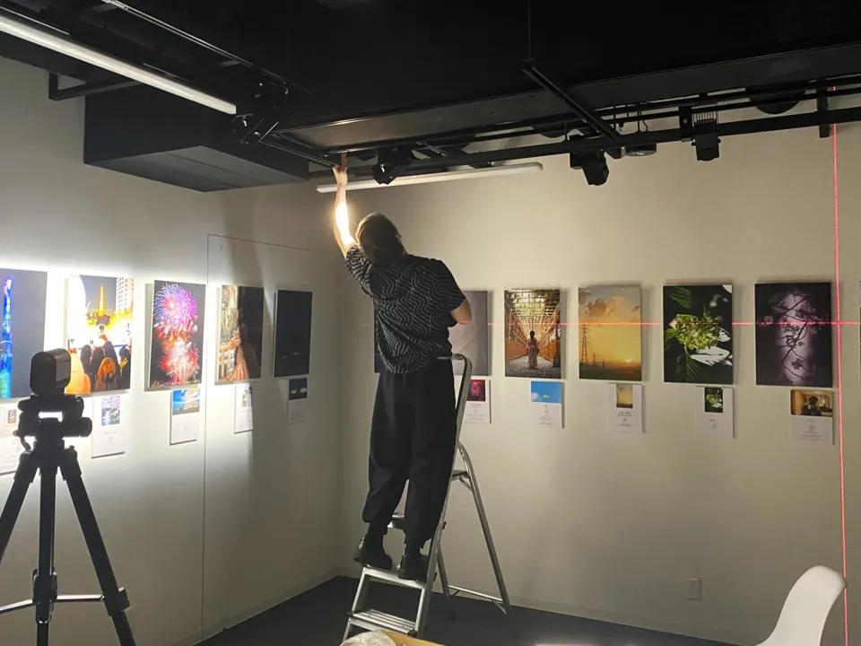 レーザー墨出し器で高さをそろえながら、写真展の照明と作品を設営するスタッフ