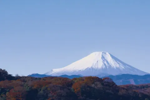 紅葉の山並みの向こうにそびえる富士山